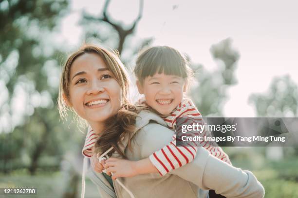 young asian mom carrying her daughter on back in park joyfully - asia kid imagens e fotografias de stock