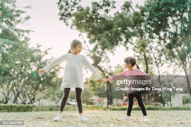lovely little sisters doing stretching exercises in park joyfully - jambes écartées photos et images de collection
