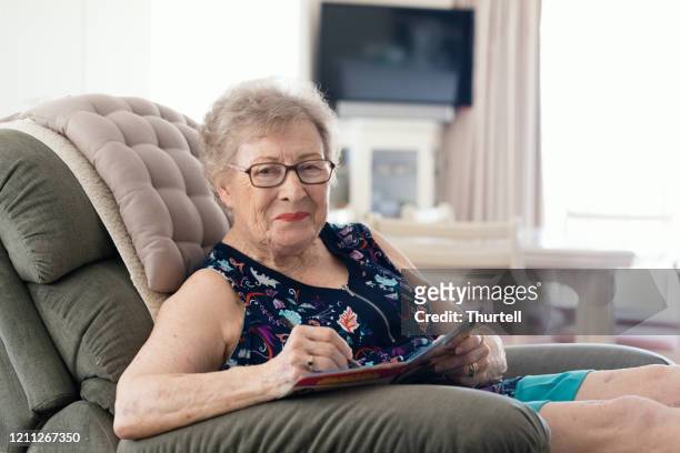 senior woman doing crossword in favourite chair - senior puzzle stock pictures, royalty-free photos & images