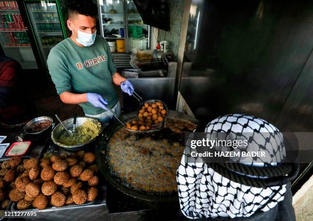 Palestinian cook, clad in latex gloves and a face mask due to the COVID-19 coronavirus pandemic, fries falafel at a local restaurant in the city of...