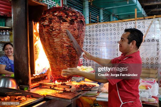 Waiter cutting portions of meat from a large shawarma that is cooking over a fire in a street restaurant in the Merida municipal market.