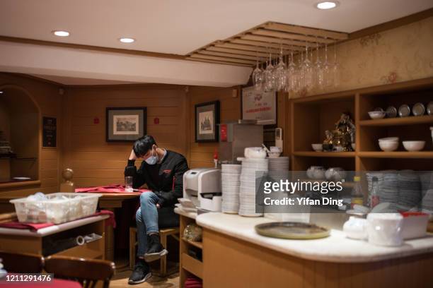 Waiter wearing a protective mask looks at a smartphone in a restaurant on March 09, 2020 in Shanghai, China. Twenty-one of mainland China's 31...