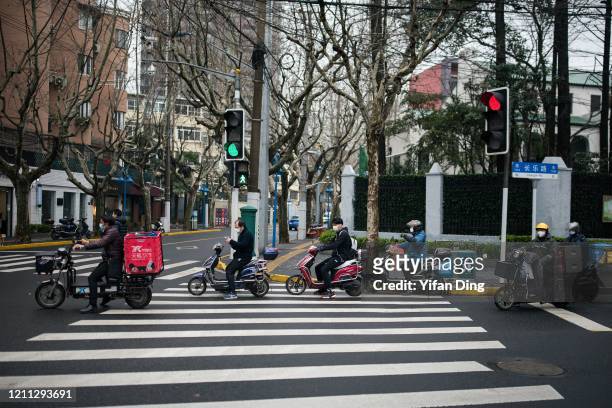Delivery service workers wearing protective masks wait for traffic light at a road crossing on March 09, 2020 in Shanghai, China. Twenty-one of...