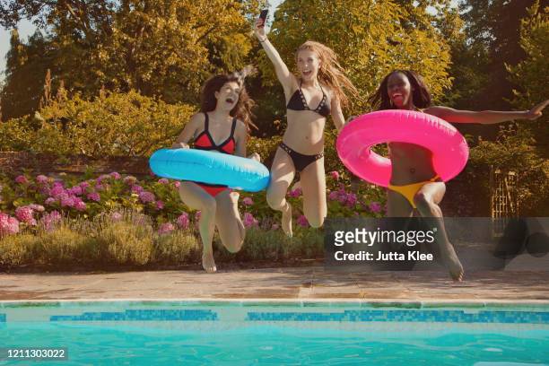 playful teenage girl friends jumping into sunny summer swimming pool - social action party stock pictures, royalty-free photos & images