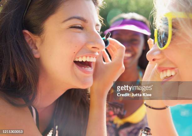 happy teenage girl friends applying mascara on sunny patio - makeup smile laugh closeup female stock pictures, royalty-free photos & images
