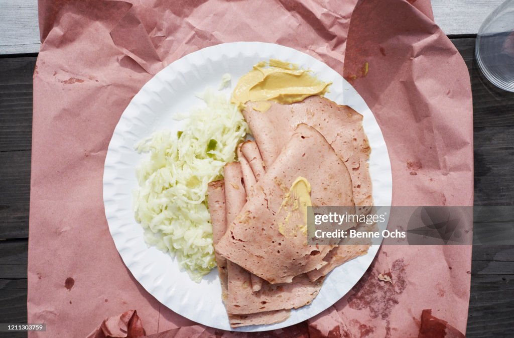 View from above ham with mustard and coleslaw on paper plate