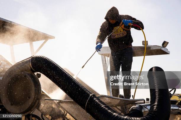 Migrant farm laborer from Fresh Harvest working with an H-2A visa hoses down a spinach harvesting machine after the night shift on April 27, 2020 in...