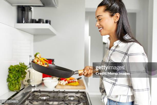 smiling woman tossing vegetables in kitchen - tos stock pictures, royalty-free photos & images