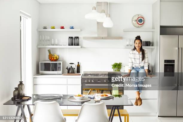 porträt einer glücklichen frau, die auf der küchentheke sitzt - appliance stock-fotos und bilder