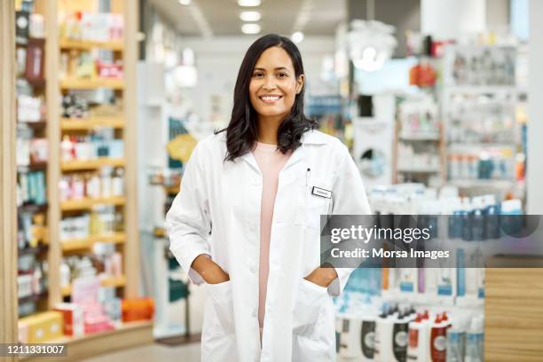 young female doctor standing with hands in pockets - apotheker blick in kamera stock-fotos und bilder