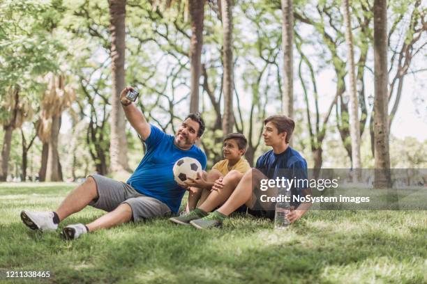 father and sons playing soccer in the park, taking selfie - football phone stock pictures, royalty-free photos & images