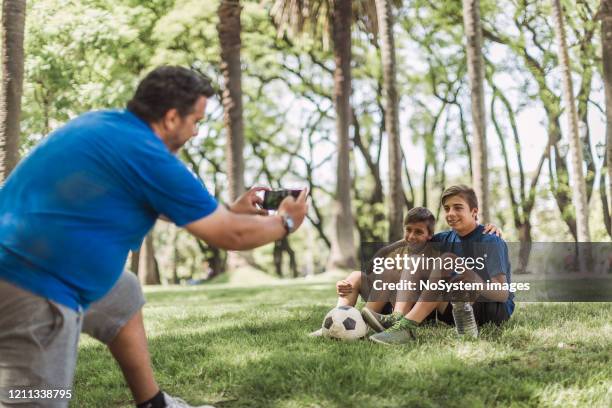father and sons playing soccer in the park - football phone stock pictures, royalty-free photos & images
