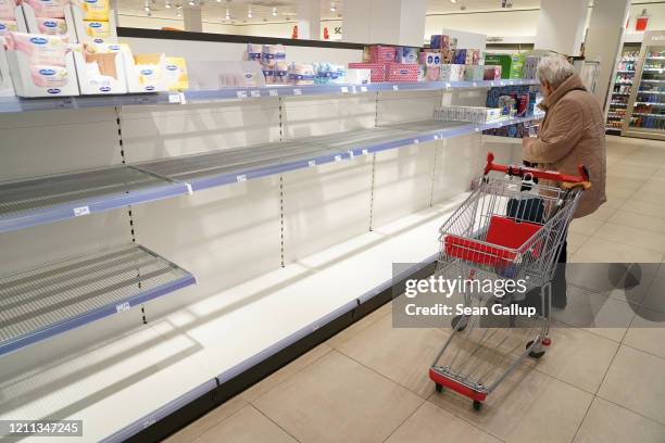 An elderly woman stands before empty shelves of sold out toilet paper and paper towels at a drug store on March 9, 2020 in Berlin, Germany. Household...