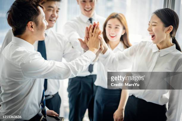 gruppe lächelnder geschäftsleute, die sich gegenseitig beim zusammenstehen in einem modernen bürogebäude hochfizieren - business people cheering in office stock-fotos und bilder