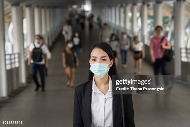 asian woman with protective face mask in the urban bridge in city against crowd of people - covid anxiety stock pictures, royalty-free photos & images