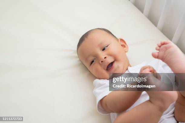6 maanden oude babyjongen ligt in zijn wieg die zijwaarts kijkt terwijl het vastmaken van zijn voeten - 6 11 maanden stockfoto's en -beelden