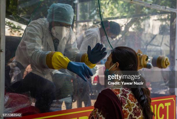 An Indian health official inside a COVID-19 mobile testing van uses a nasal swab to collect a sample from a woman, as India remains under an...