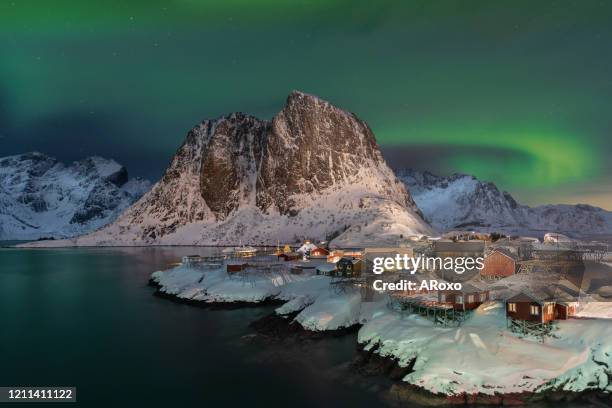 aurora boreal over the small fishing village with its traditional red huts. beautiful northern lights in hamnoy, lofoten island in norway. - aurora borealis lofoten stock-fotos und bilder