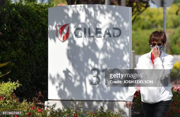 Woman wearing a mask walks by Gilead Sciences headquarters sign in Foster City, California on April 30, 2020. Gilead Science's remdesivir, one of the...