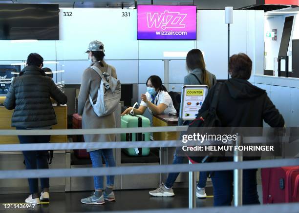 Flight passengers queue at a check in desk of the low-cost airline Wizz Air on May 1, 2020 at the Schwechat airport near Vienna, Austria. - Wizz Air...