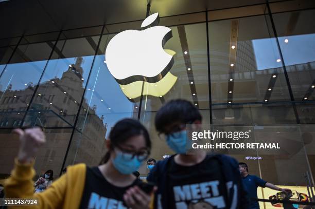 People wearing face masks look at a cellphone outside an Apple store during a May Day holiday in Shanghai on May 1, 2020. - With optimism and a heavy...