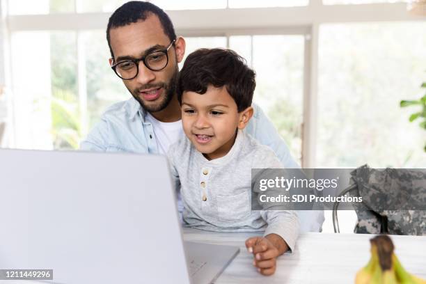 mid adult dad and his son watch something on laptop - handsome military men stock pictures, royalty-free photos & images