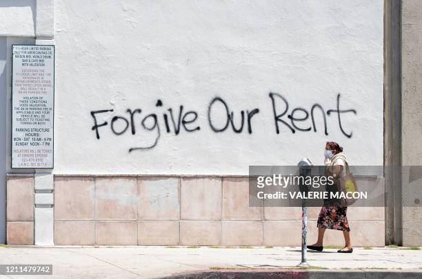 Woman wearing a mask walks past a wall bearing a graffiti asking for rent forgiveness on La Brea Ave on National May Day amid the Covid-19 pandemic,...