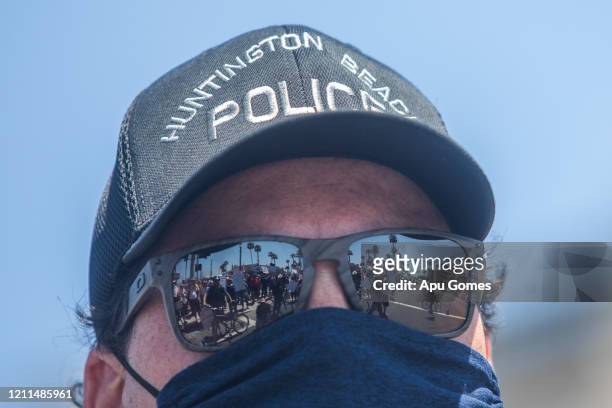 Police Officer wears a face scarf as a preventive measure against the spread of the COVID-19 Coronavirus while watches protesters gathering in a...