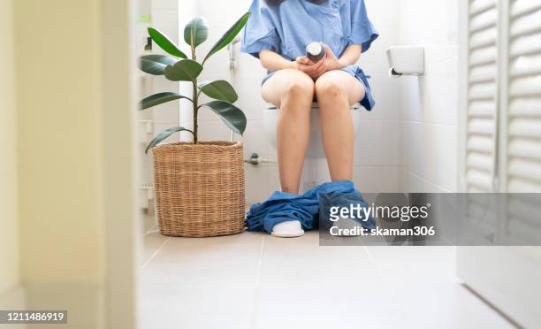 asian female sitting in toilet and holding medicine bottle for stomach problem - hemorrhoid - fotografias e filmes do acervo