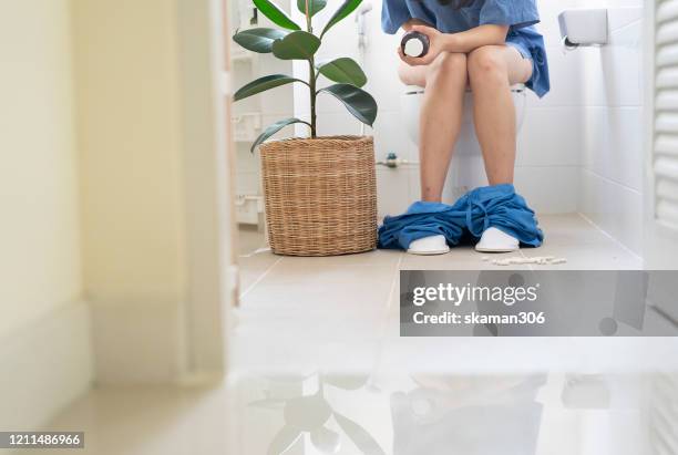 asian female sitting in toilet and holding medicine bottle for stomach problem - diarrhoea foto e immagini stock
