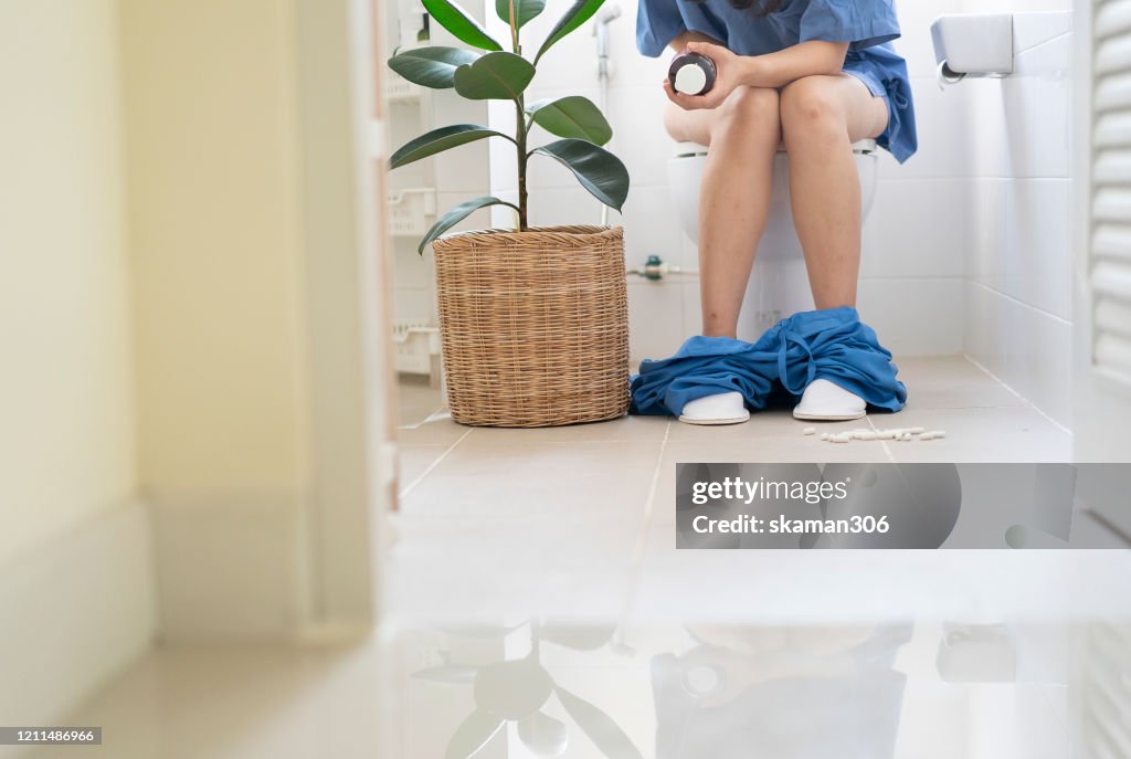 Asian female sitting in toilet and holding medicine bottle for stomach problem