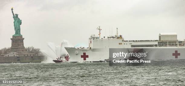 On a gloomy rainy day USNS Comfort hospital ship leaves New York City in front of Statue of Liberty after treating some patients during COVID-19...