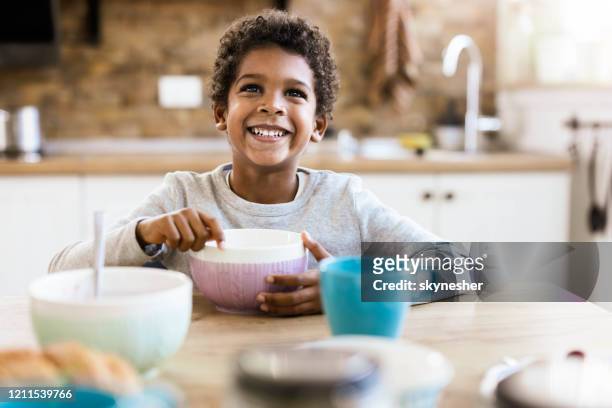 felice ragazzo nero che mangia la sua colazione al tavolo da pranzo. - boy eating cereal foto e immagini stock
