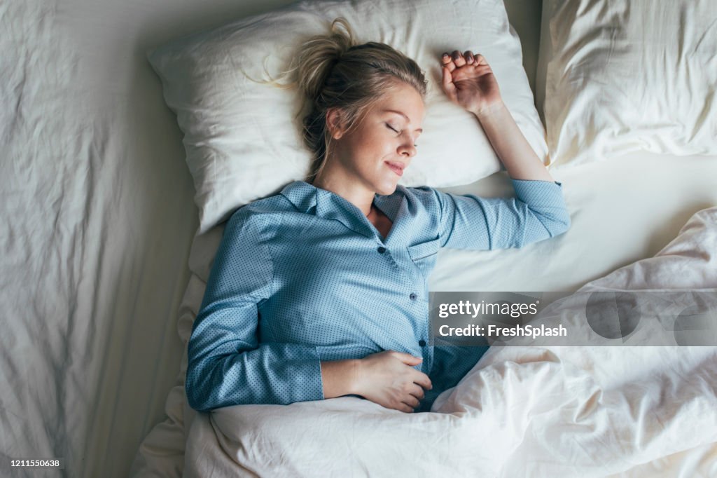 Sonido Dormido: Tiro de cintura superior de una mujer rubia bonita en pijama azul durmiendo en una cama King Size