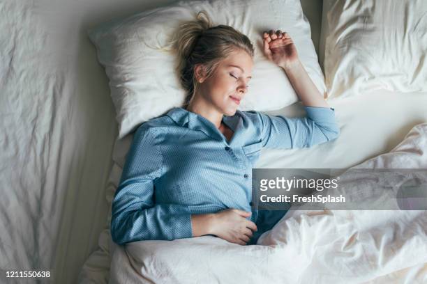 sound asleep: overhead waist up shot of a pretty blonde woman in blue pyjamas sleeping on a king size bed - duvet stock pictures, royalty-free photos & images