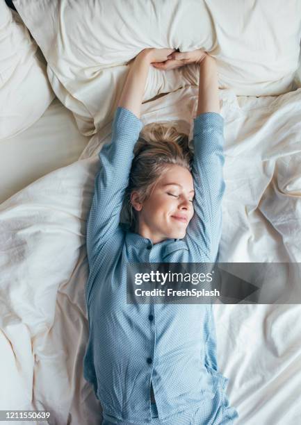 weekend mornings: happy blonde woman in blue pyjamas stretches after waking up - woman waking up happy stock pictures, royalty-free photos & images