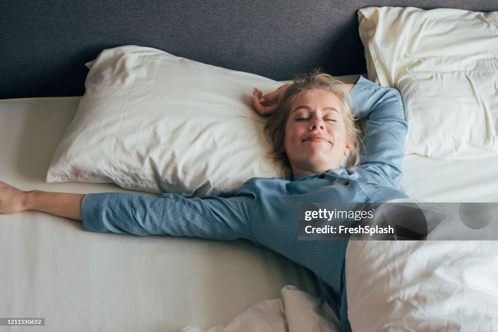 Feeling Energized: Happy Blonde Woman in Pyjamas Stretches in Bed after Waking Up in the Morning