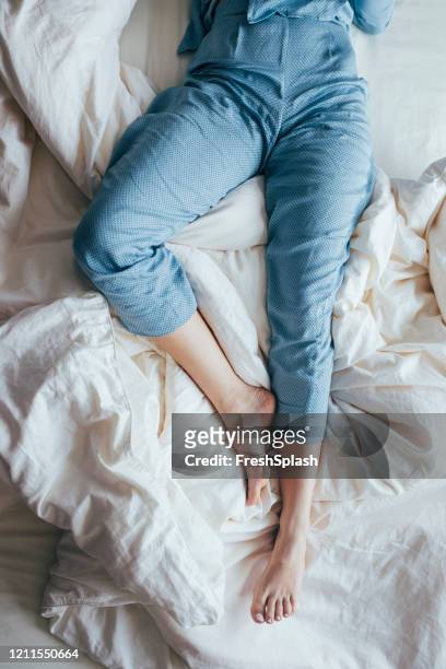 waist down shot of legs of a woman in blue pajamas sleeping on bed, overhead view - nightwear stock pictures, royalty-free photos & images