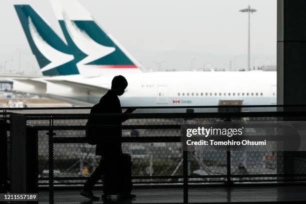 Passenger wearing a face mask walks past Cathay Pacific aircraft parked at Kansai International Airport on March 10, 2020 in Osaka, Japan. The...