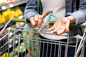 Asian shopper disinfecting hands with sanitizer in supermarket during shopping