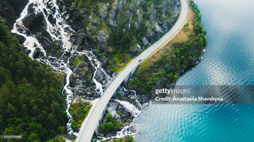 Vista aérea da estrada montanhosa panorâmica com carro, mar e cachoeira na Noruega
