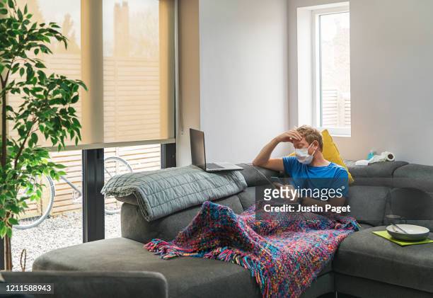 man in self isolation on the sofa with the flu - illness stock pictures, royalty-free photos & images