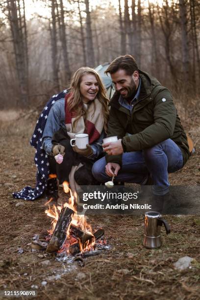 happy couple is roasting marshmallow and enjoying their camping adventure - blanket stock pictures, royalty-free photos & images