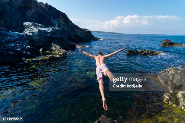 zwei junge männer springen von klippe ins meer - diving risk stock-fotos und bilder