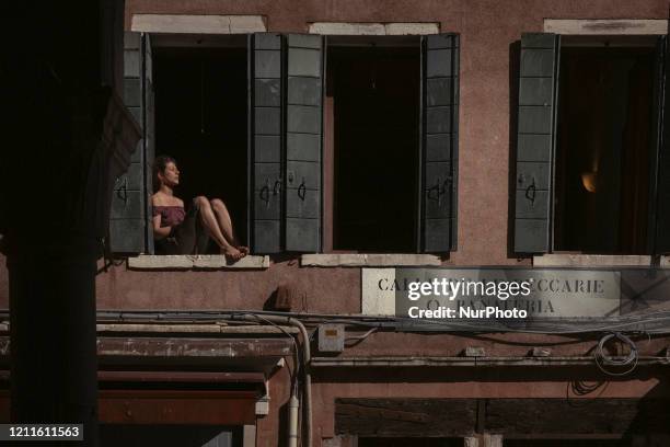 A woman looking out onto her balcony on Calle delle Beccarie sunbathing, Venice, Italy, 1th May 2020 during the coronavirus emergency.