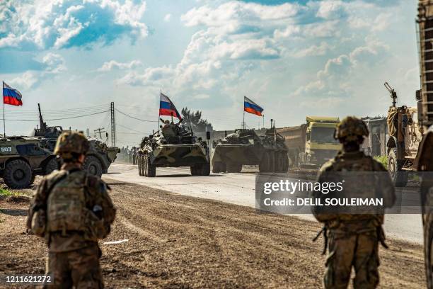 Soldiers stand along a road across from Russian military armoured personnel carriers , near the village of Tannuriyah in the countryside east of...