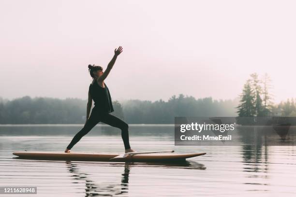 jonge vrouw die yoga op een paddleboard praktizert - practioners enjoy serenity of paddleboard yoga stockfoto's en -beelden