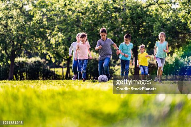 groep kinderen die voor sportbal in openbaar park lopen - club de fútbol stockfoto's en -beelden
