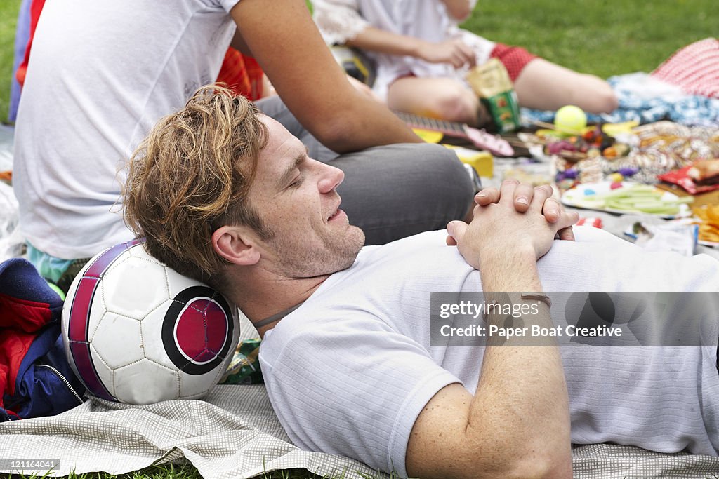 Man resting his head on a football in park at bbq
