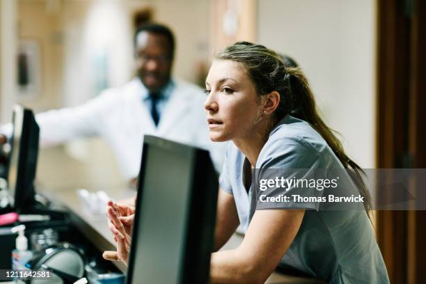 nurse leaning on counter at nurses station in hospital - schwesterntisch stock-fotos und bilder